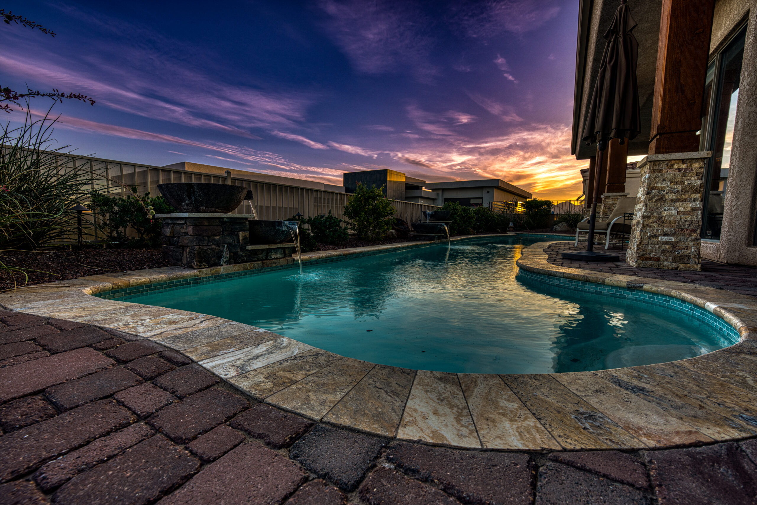 Curved backyard pool with stone deck and water features at twilight in Lake Havasu home