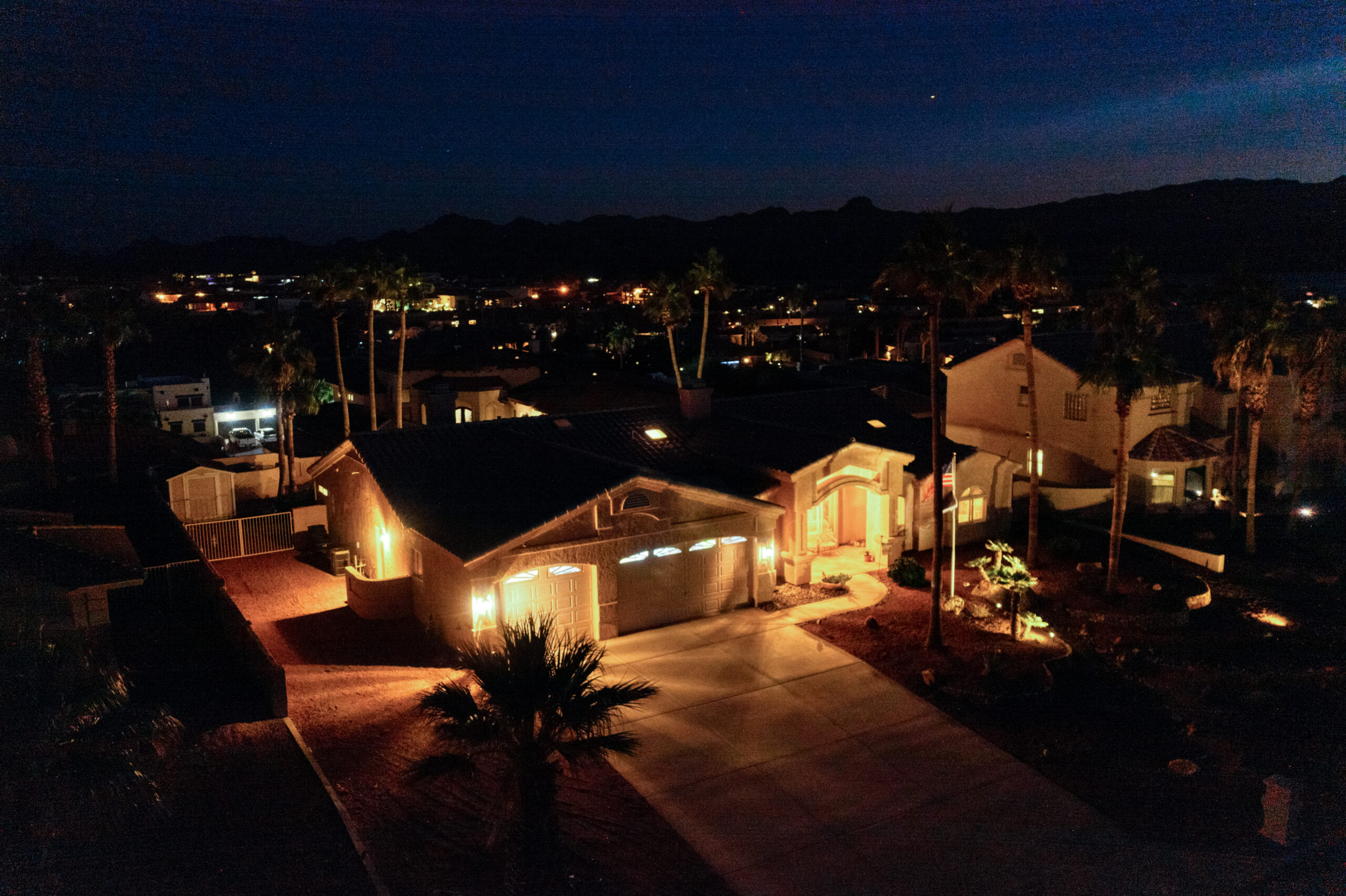 Front exterior of luxury home at night with architectural lighting captured by drone in Lake Havasu