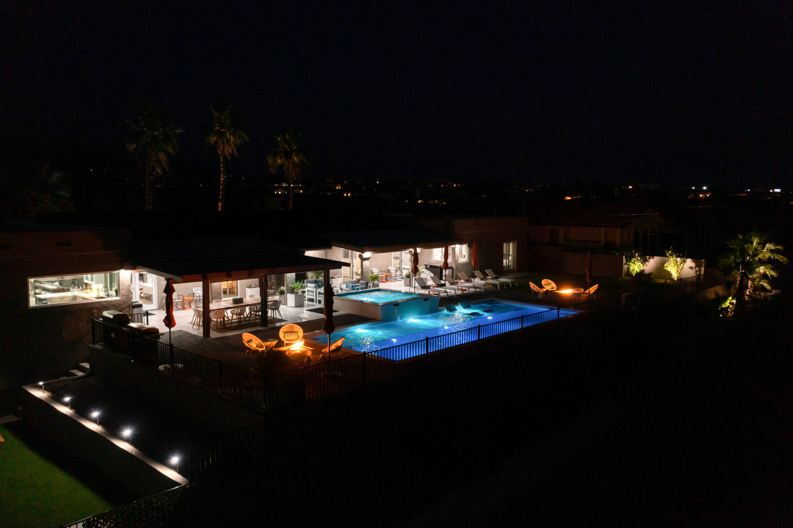 Luxury Lake Havasu home at night with illuminated pool, firepit, and outdoor living space captured by drone