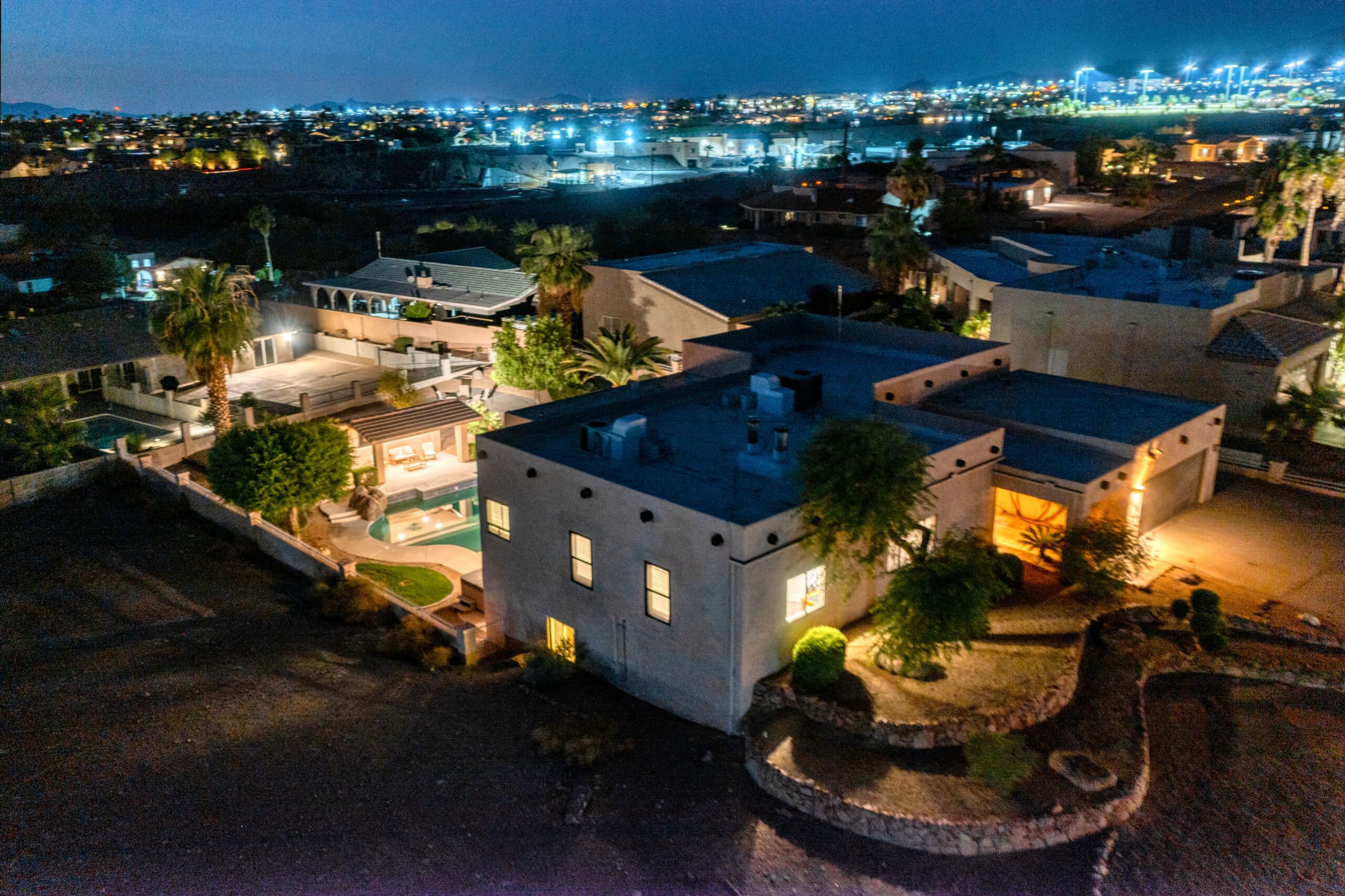 Luxury home twilight aerial in Lake Havasu City featuring pool, backyard lighting, and desert landscape