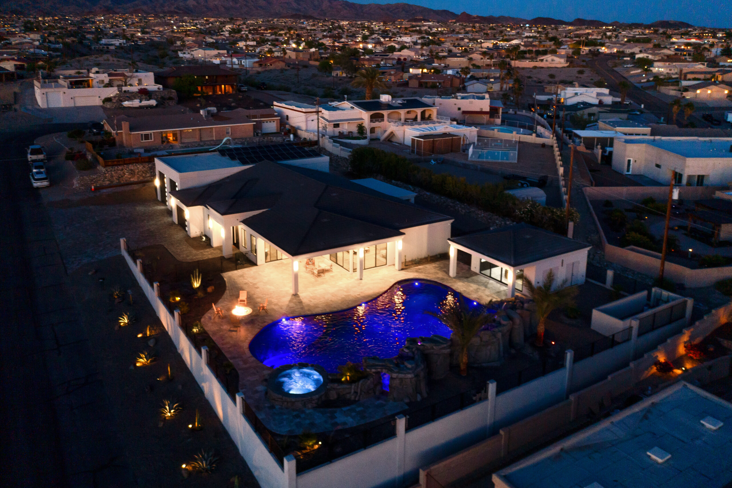 Twilight drone aerial of modern Lake Havasu home with illuminated pool and outdoor living space