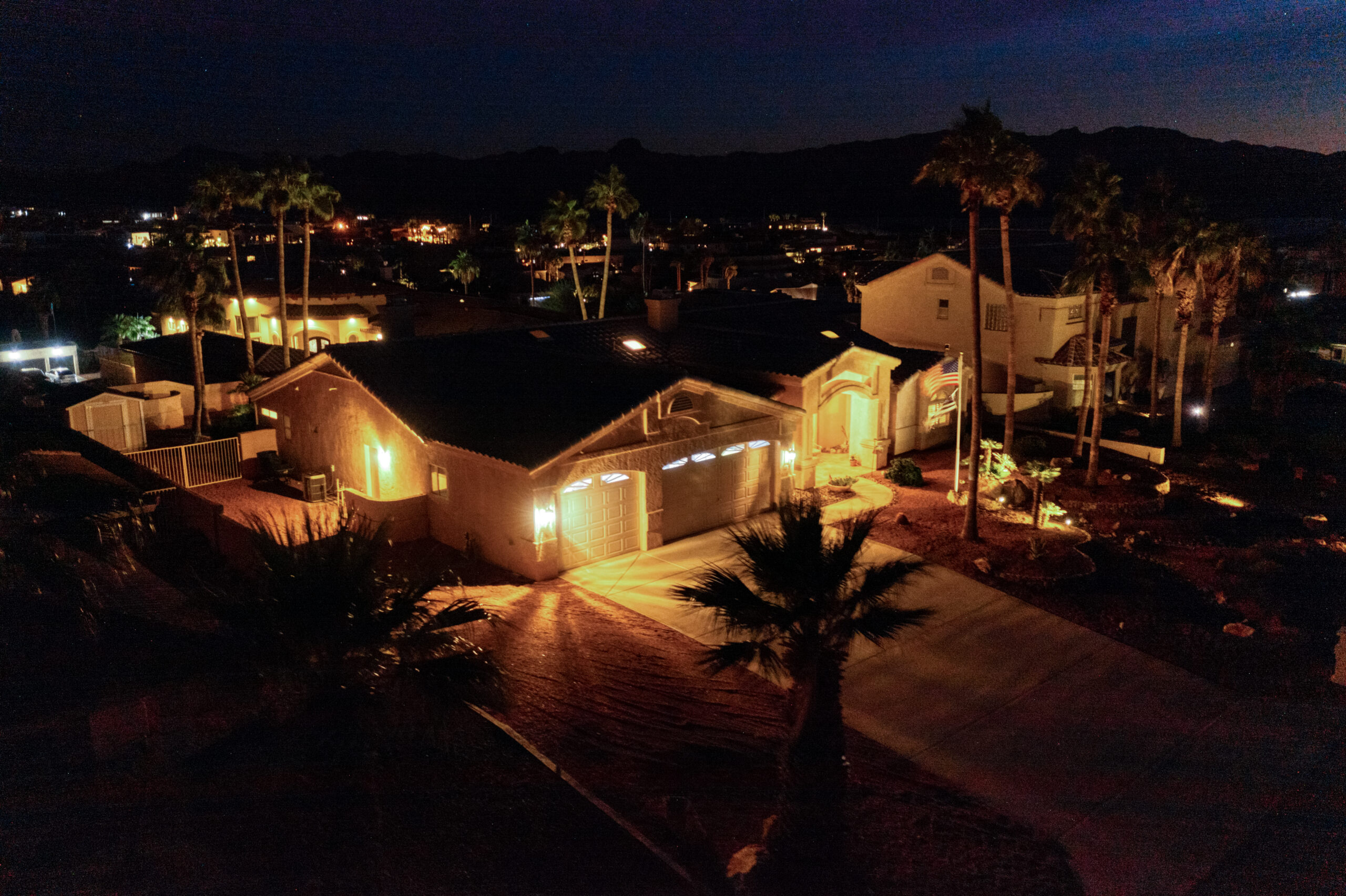 Aerial night view of luxury home with glowing blue pool and landscape lighting in Lake Havasu